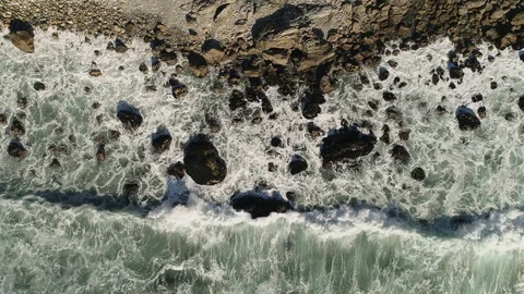 Static birds eye view straight down of rocky shoreline with waves crashing. Video stock 87963628