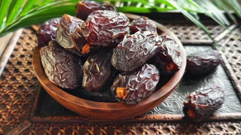 Static close up of date fruit in wooden bowl with moving palm leaf and soft.. Stock Footage 339080896