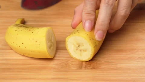 Static Close Up Hand Cutting Unpeeled Yellow Banana On Board 4K Stock Footage 322140296