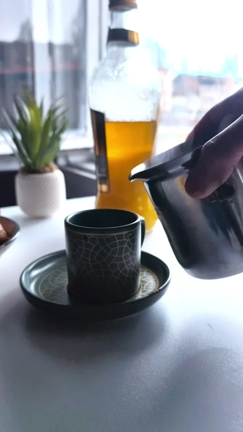 Static close-up shot of a hand pouring steaming hot coffee from a metal pitcher Vídeos de archivo 334700251