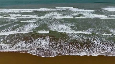 Static drone shot of the ocean with calm waves reaching the shore of a white Stock Footage 284444256