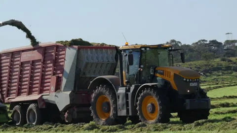 Static ground shot of passing tractor &amp; chopper working in a field loading Video stock 138768281
