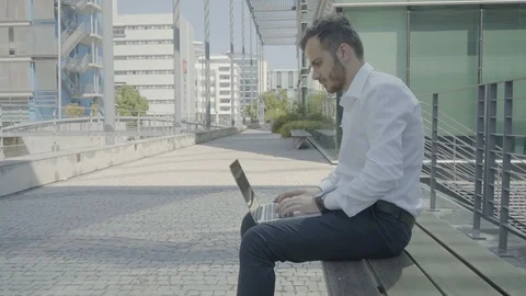 Static long shot of young Caucasian man with laptop on bench Stock Footage 97923375