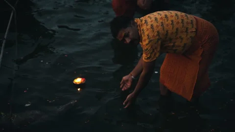 Static medium shot of devotee setting floating oil lamp on Ganges river in Vidéo 348108867