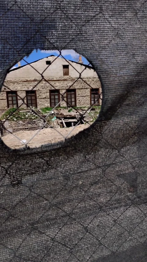 Static shot of an ancient stone house viewed through a hole in a wire fence. Vídeos de archivo 333908390