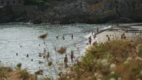 Static shot of crowded beach with swimmers, rocky cliffs, overcast sky, summer Stock Footage 341314432