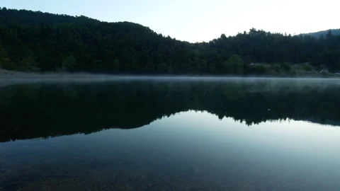 Static shot of dark lake reflective waters with morning fog on the surface Video stock 131229397