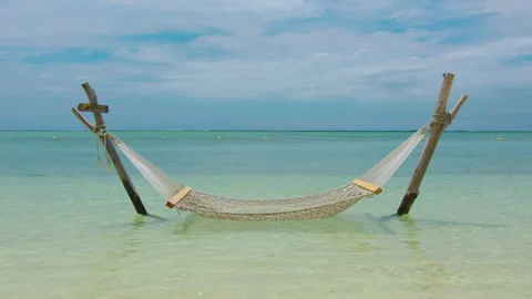 Static shot of an empty hammock slowlying by the wind with calm waves reaching Stock Footage 168052017