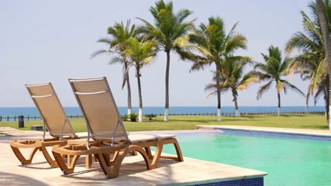 Static shot of generic beach resort with poolside beds, pool, palm trees and sea Stock Footage 185616115