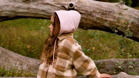 Static shot of girl sitting on fallen tree in forest clearing during autumn Stock Footage 346622487