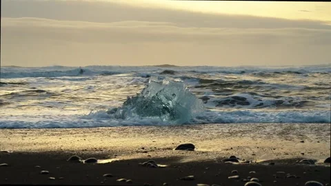 Static shot of a large ice diamond on black sand beach with crashing waves .. Stock Footage 327683723