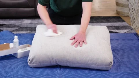 Static Shot Man Cleans Stained Pillow by Pouring Cleaner on Rag and Scrubbing Stock Footage 307823564