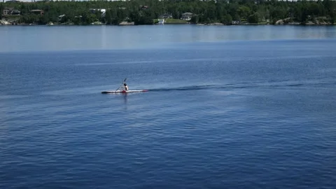 Static shot of a man kayaking across water from right to left Stock Footage 200790367