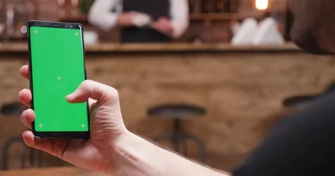 Static shot of man working and scrolling on a phone with green screen Stock Footage 104496475