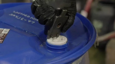 Static shot overcast factory worker opening coolant drum cap in France Stock Footage 336613079