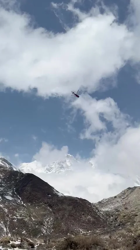 Static shot of a red helicopter flying in the blue sky above snow covered m.. Video stock 337449144