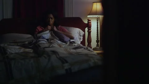 Static shot of a scared woman sitting on bed staring at her door Stock Footage 202907310