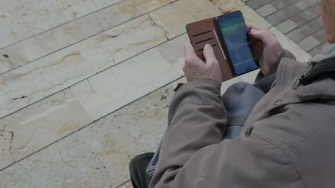 Static shot on senior man seated outdoor on a bench and using his cellphone. Stock Footage 122314142