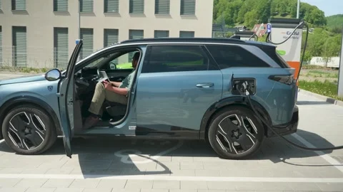 Static Shot Sunny Day Man Working on Tablet in Charging Peugeot 5008 EV Germany Stock Footage 334826545