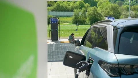 Static Shot Sunny Day Software Engineer Works on Laptop at EV Charging Station Stock Footage 334825837