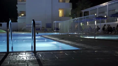 Static shot of swimming pool at night with people taking a dip in the backgro Stock Footage 142403313