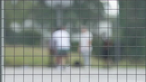 Static shot through a metal fence of people playing basketball on an outdoor cou Stock Footage 136581604