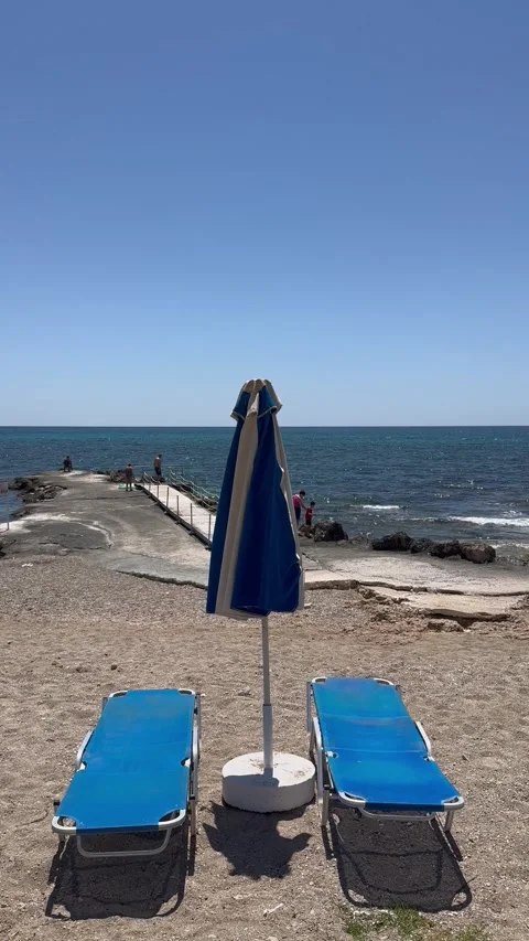 Static shot of two blue sunbeds and an umbrella on a sandy beach by the sea Stock Footage 336320323
