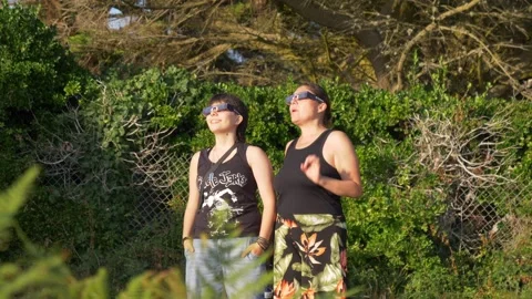 Static shot of two women wearing eclipse glasses gazing upward on sunny day Stock Footage 346454802