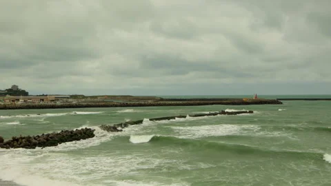 Static shot of waves rolling toward harbor breakwater in Japan on overcast day Stock Footage 321106030