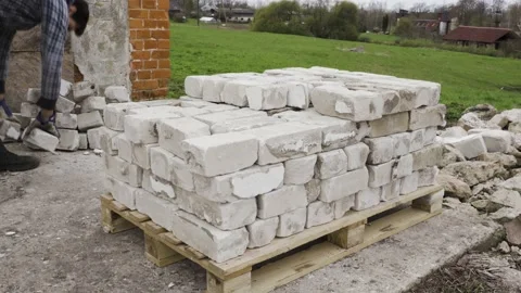 Static shot of a worker piling used fly ash bricks on a pallet Stock Footage 154941380
