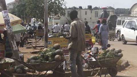 Static tight shot of pineapple vendor at Ugandan market with light cross traffic Video stock 81749109