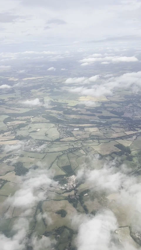Static vertical shot of green countryside through scattered clouds from airplane Video stock 336512167