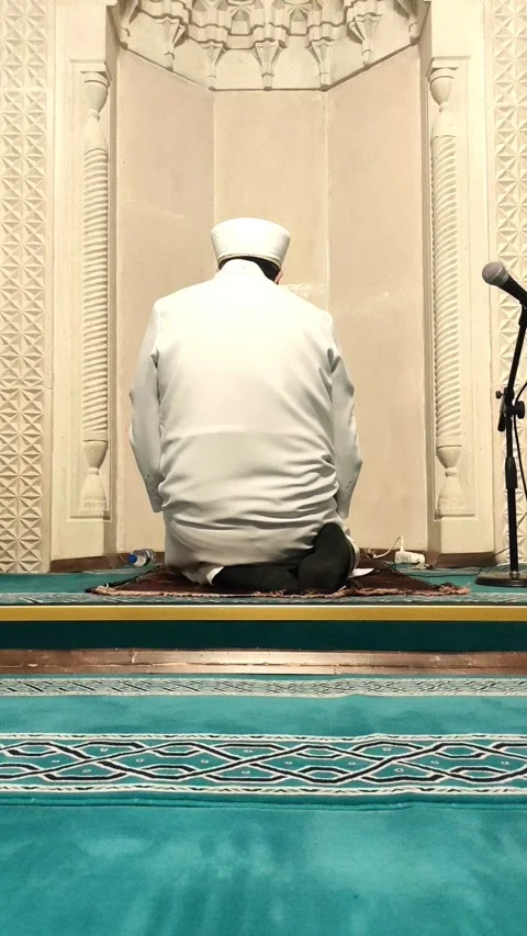 Static vertical shot of an Imam in white traditional clothing sitting in prayer Vídeos de archivo 333605926