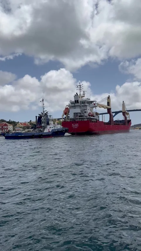 Static vertical shot of a red cargo vessel from behind towing a small boat Stock Footage 336656550