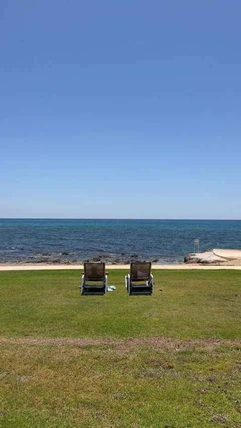 Static vertical shot of two chairs on a green lawn by the ocean Stock Footage 336320470