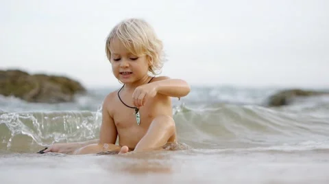 Static view of little cute smiling child playing with shells in blue sea. Stock Footage 52931460