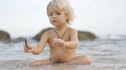 Static view of little cute smiling child playing with shells in blue sea. Stock Footage 52931682