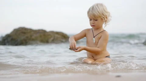 Static view of little cute smiling child playing in blue sea with shells Stock Footage 52931993