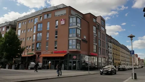 Static view of street corner with shops, cars and people against sky Stock Footage 200894247