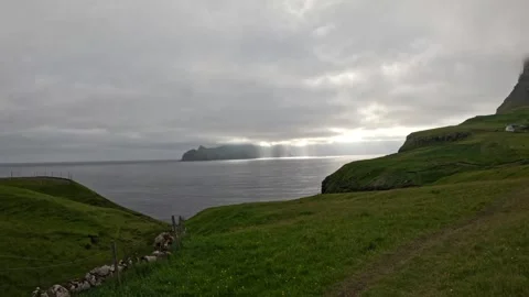 Static wide shot of green cliffs and sun rays over ocean, Faroe Islands Stock Footage 337558560