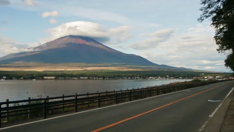 Static wide shot of lakeside road with Mount Fuji above Lake Yamanaka in Japan Stock Footage 321127737