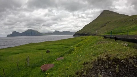 Static wide shot of a misty green hill and ocean bay next to a highway guardrail Vidéo 340009028