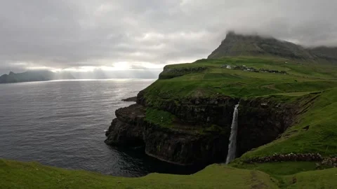 Static wide shot of Mulafossur waterfall and Gasadalur village in dramatic light Stock-Footage 337558561