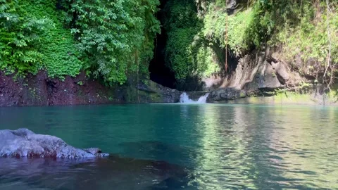 Static wide shot of a serene emerald lagoon and hidden cave waterfall in Bali Stock Footage 336904319