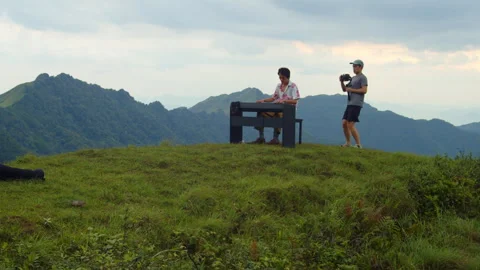 Static Wide Shot of Videographer Orbiting Asian Piano Player on Mountain Peak Stock Footage 340396248