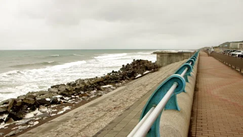 Static wide shot of waves hitting rocky seawall along an empty coastal promenade Stock Footage 321104918