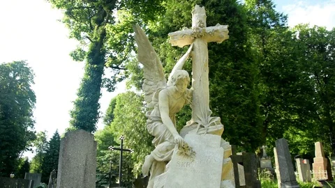 Statue of an angel with a cross looking down on a background of trees Video stock 115033487