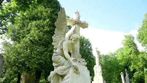 Statue of an angel with a cross looking down on a background of trees 스톡 동영상 115194804