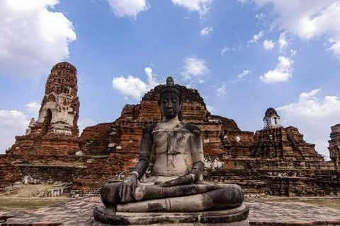 A statue of Buddha is sitting on a stone platform in front of a large buildin Stock Photos