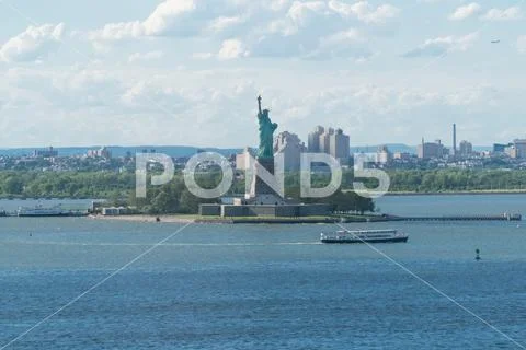 Statue of Liberty stand tall over New York City harbor on clear summer day Stock Photos